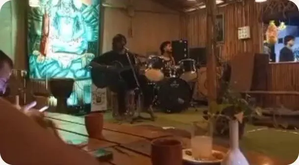 A guitarist and drummer playing live in a warm wooden room